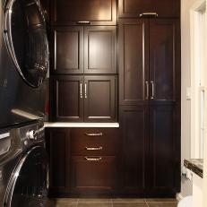 Traditional Laundry Room Design With Dark Wood Cabinets and Stacked Washer and Dryer 