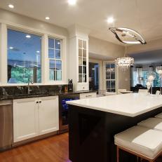 Black and White Island With Leather Barstools in Contemporary Kitchen Featuring Black Marble Countertop and Stainless Steel Light Fixture 