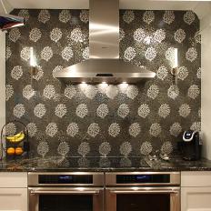 Floral Pattern Tile Backsplash Framed By Glass Door Cabinets Over Side-by-Side Ovens With Stainless Steel Range Hood