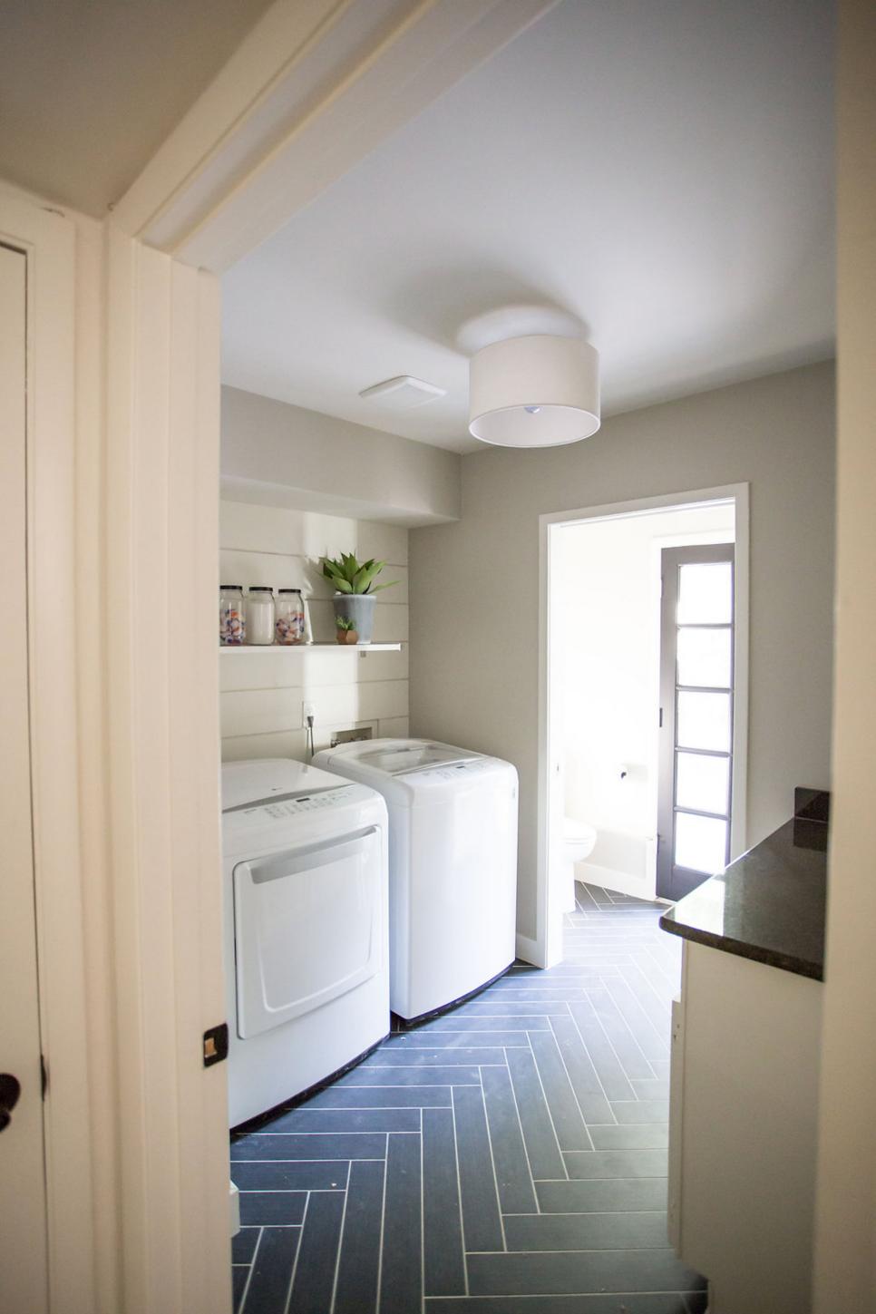 Spacious Laundry Room With Black Tile Floor, Floating Shelf and Side-By