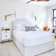 Sunlight Floods The White Master Bedroom Featuring Gold Sconces, Upholstered Headboard and Textured Area Rug 