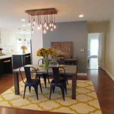 Warmly Lit Midcentury Modern Dining Room With Modern Pendant Chandelier, Yellow Rug and Sunflower Centerpiece 