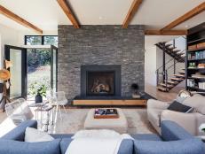 Cozy Contemporary Living Room With Large, Textured Rock Fireplace Surround and Exposed Wood Ceiling Beams