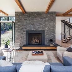 Cozy Contemporary Living Room With Large, Textured Rock Fireplace Surround and Exposed Wood Ceiling Beams