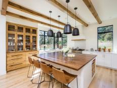 Large Kitchen Eat-In Island With Brown Leather Bar Chairs and Polished Wood Countertop Under Black Pendant Lights 
