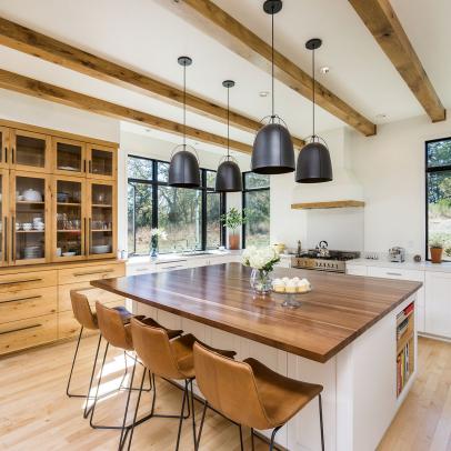 Large Kitchen Eat-In Island With Brown Leather Bar Chairs and Polished Wood Countertop Under Black Pendant Lights 