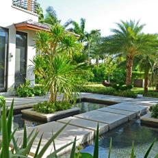 Concrete Walkway Over Pond in Tropical Yard With Bright Plant Life 