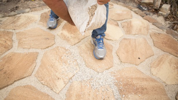 Once the area is dry, pour pea gravel out in small sections and sweep across the surface of patio until the gaps between pavers and border stones are filled and level