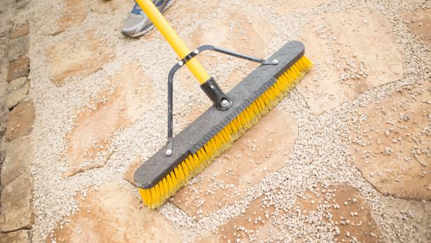 Once the area is dry, pour pea gravel out in small sections and sweep across the surface of patio until the gaps between pavers and border stones are filled and level
