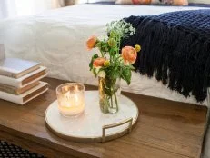 The master bedroom's primitive bench at the end of the bed, has deorative flowers and a candle, as seen on Fixer Upper. (After)