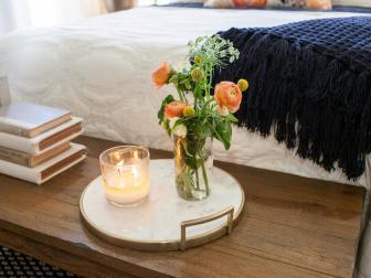 The master bedroom's primitive bench at the end of the bed, has deorative flowers and a candle, as seen on Fixer Upper. (After)