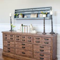 Wooden Country Dresser Decorated With Tall Candlesticks and Antique Book Ends Under Mounted Metal Shelf