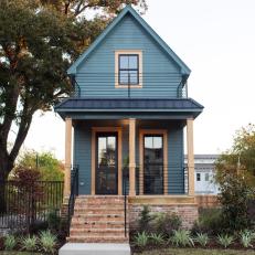 Bold Dark Green Vintage Tiny Home with Wrap Around Brick Skirt ,Unpainted Wood Columns, Iron railing and Metal roof 