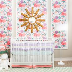 A Stylish Nursery's Floral Panels and Gold Sunburst Mirror Frame the Crib