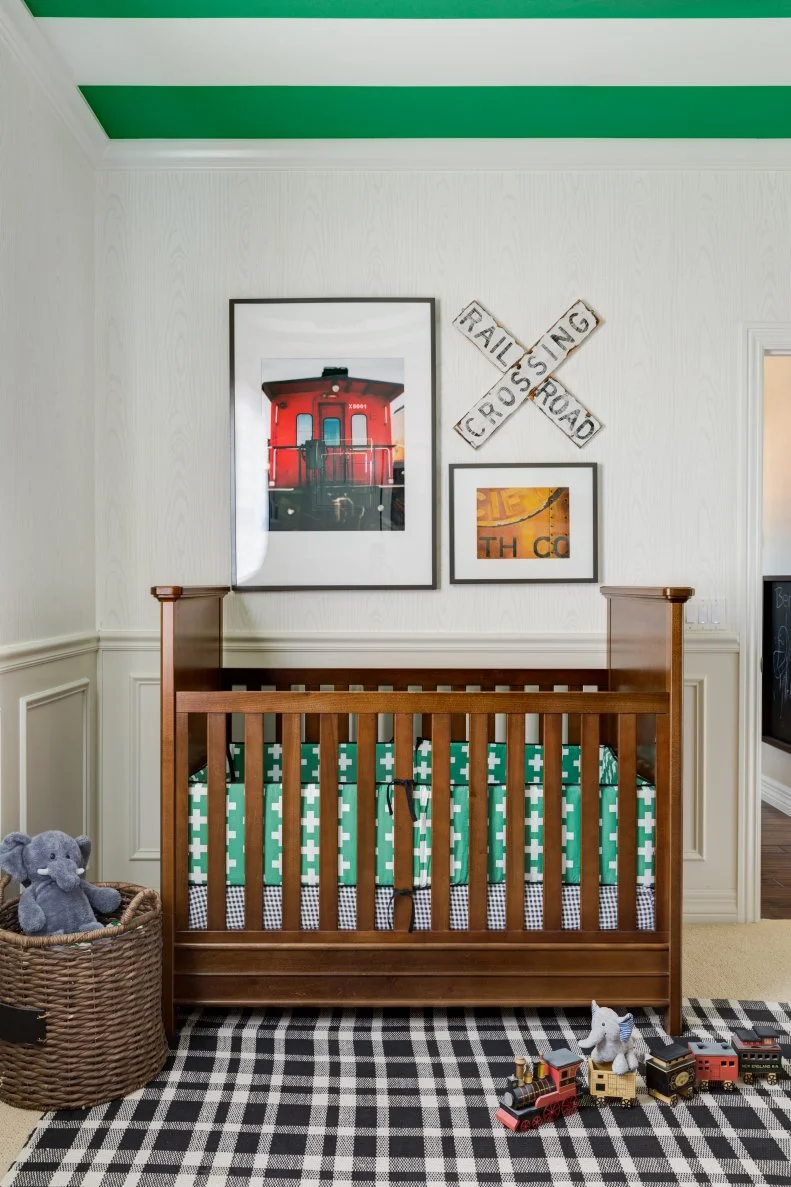 Train artwork sits above a crib and plaid rug sits below in a nursery.