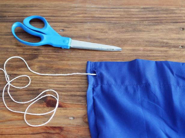 Cut a small slit in the top left corner and the top right corner of the sheet; be sure to only cut through one layer of fabric in the hem. Tie a few knots at the end of the rope, then thread the rope through the top left slit.
