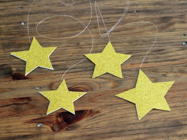 Paint the wooden stars white and glue to the sheet, along the ridge created by the hula hoop. For each hanging star, cut two of the same star from either the gold glitter paper or the gold metallic paper. Using double-sided tape, attach the two stars back to back with a length of fishing line in between. Tape the fishing line to the inside of the canopy so the stars hang at various lengths.