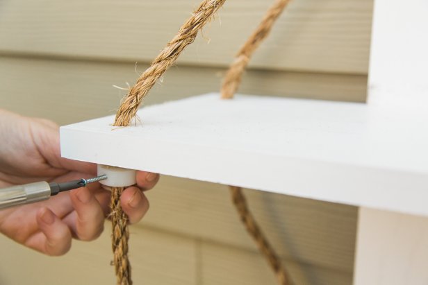 It’s important to take the time to get the top shelf adjusted so that it’s the desired height with the back rope first. Once you determine the proper height of the top shelf on the rope, drive the small #4 ¾ inch screws into each grommet slowly with a drill or by hand with a phillips head screwdriver, pushing the screw through the back rope and into the other side of the grommet. Since you used the countersink bit, the screw should lay flat and the grommet will slide nicely up into the hole you drilled into the underside of the board, out of sight. Repeat this step on the other side of the shelf/back rope. Next, focus on the front ropes and getting the top shelf completely level before moving on, driving screws into the grommet/rope, then sliding the shelf down onto the grommet so that the shelf is proper height and level. Once you get it “just so” you can measure down from this top shelf to get the lower shelves spaced correctly and level, as well.