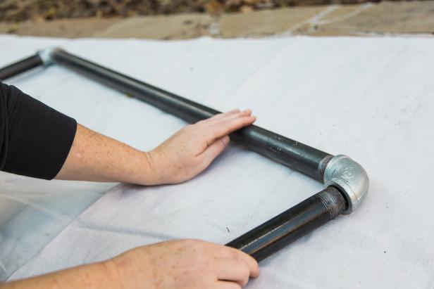 Once any stickers and excess oil are removed from the galvanized pipe, lay it down and attach the two elbows to each end of the 36” piece, then attach the two 5 ft. pieces to those elbows-creating an upside down “U” shape.