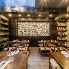 Plate Accent Wall Framed With Black Subway Tile In Public Dining Room With Wood Tables and Built In Shelving 