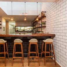Contemporary Public Bar With White Subway Tile Wall, Black Subway Tile Bar With Wood Countertop and Tall Wood Barstools
