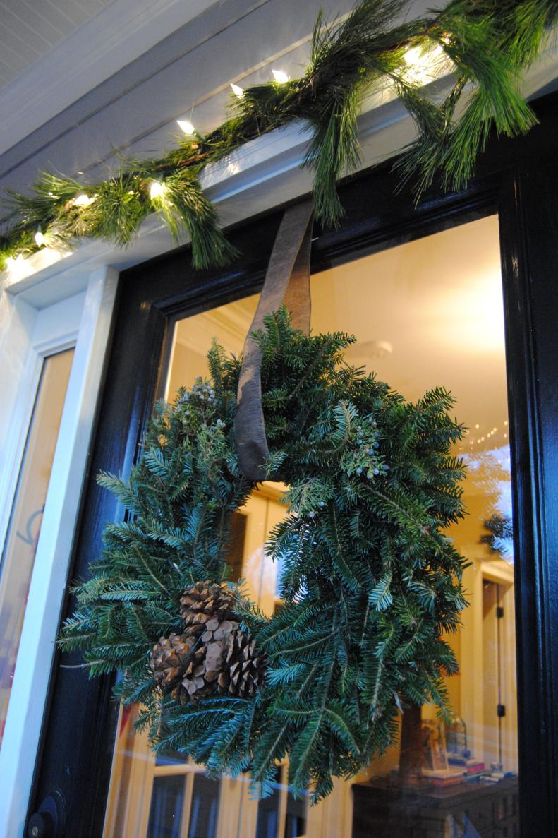 After: A fresh Fraser fir wreath from Trader Joe's ($9.99) came with pine cones, which we also used inside. The wreath has the same mix of greenery as the swags but instead of a red ribbon, Ashley Aquino snipped a piece of wide brown ribbon (used inside the home) to loop around the wreath. A clear Command Hook holds the wreath on the glass, and the ribbon is simply taped at the top of the door.