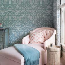 Plush Pastel Pink Chaise With Floral Throw Pillow Next to Patterned Blue Wallpaper and Natural Wood Table 
