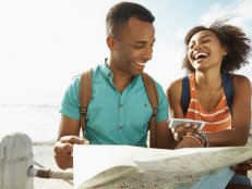 A young couple sitting on the promenade at the seaside while looking at a map