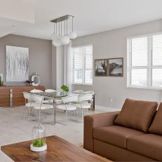 Open Gray Living Space With Brown Sofa, Glass Dining Table With White Leather Chairs and Light Hardwood Floor 