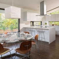 Sunny Modern Kitchen and Dining Space With Glass Dining Table, Sleek White Cabinetry and Contemporary Dining Chairs 