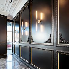 Sophisticated Lobby Highlighting Black Paneled Walls With Gold Trim, Corner Embellishments and Two Pronged Sconces  