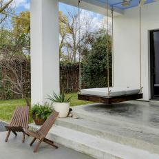 Covered Porch With Blue Painted Ceiling Over Hanging Bed Swing and Concrete Steps Leading to Wooden Outdoor Chairs 
