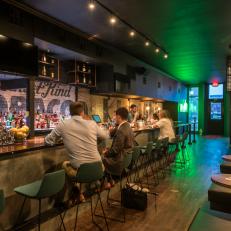 Long, Contemporary Bar Space With Green Bar Chairs, Green Neon Decorative Lighting and Leather Bench Seating 
