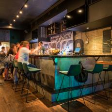 Hip, Casual Bar With Green Contemporary Barstools, Painted Brick Accent Wall and Built In Upper Cabinetry 