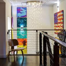 Upstairs Hallway With Dark Hardwood Flooring and Modern Wood Chair Overlooking Bold, Colorful Wall Art 