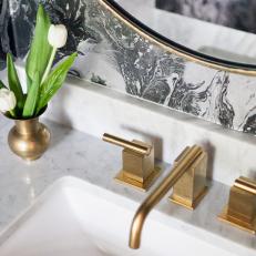 Close Up On Powder Room Vanity Sink With Brass Details Accented Against A White Marble Countertop and Black and White Wallpaper