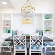 Coastal Dining Room With Dark Wood Table, White Chairs With Patterned Blue Cushions and Bench Seat With Surrounding Shelves