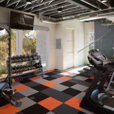 Home Gym With Black, Gray and Orange Square Carpet, Glass Lined Staircase and Exercise Machines 
