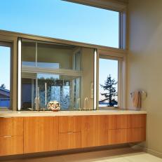 Floating Double Vanity With Thick Neutral Countertop Over Wood Cabinets and Windows Framing the Large Mirror 