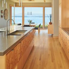 Textured Wood Cabinets, Neutral Island Countertop and Stainless Steel Pendant Lights in Modern Kitchen 