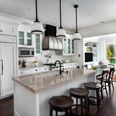 Open, Traditional Eat In Kitchen With Blended Refrigerator, Pendant Lights, and Wood Barstools At Neutral Marble Bar