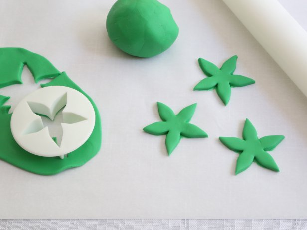 Roll the green ready-made fondant to 1/4-inch thickness with a rolling pin and cut out flower shapes using a fondant cutter. You can also cut a free-hand a flower shape from the fondant using a small knife.