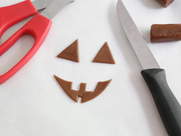 Cut pumpkin face shapes from the candy using a knife or kitchen-dedicated scissors.