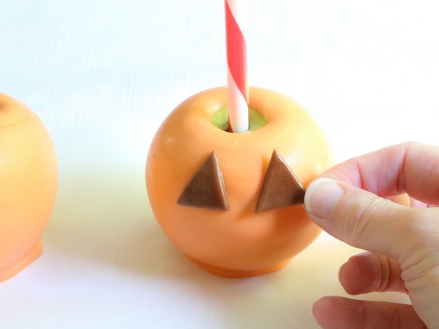 Lightly brush the backs of the pieces with corn syrup and arrange the pieces onto the apples so that a jack-o-lantern face is achieved.