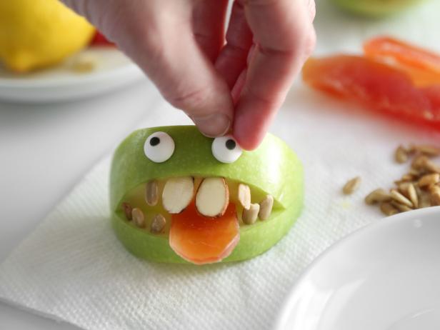 Use small dots of frosting or piping gel to on the backs of the candy eyeballs; affix just above the mouth on the apple skin.
