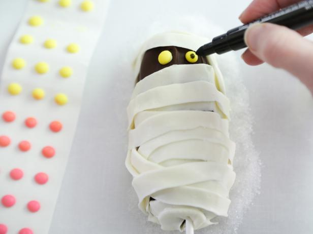 Use dots of frosting on the backs of the candy dots and affix them on the chocolate portion at the top 1/4 of the cake. Draw dots onto the dots using a food color marker or a paint brush dipped in food color.