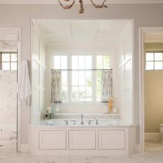 Large Bathtub in Window Nook of Bright Master Bathroom With White Marble Tile and Simple Decorative Wall Design 