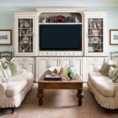 Cozy Shabby Chic Family Room Featuring Neutral Sofas With Ruffles Skirts and Large Entertainment Center With Mullion Cabinets