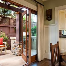 Large French Doors Opening From Dining Room to Concrete Patio With Wood Retaining Wall and Decorative Bench 