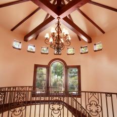 Crossed Wood Beams With Traditional Chandelier Over Grand Staircase With Wrought Iron Banister 